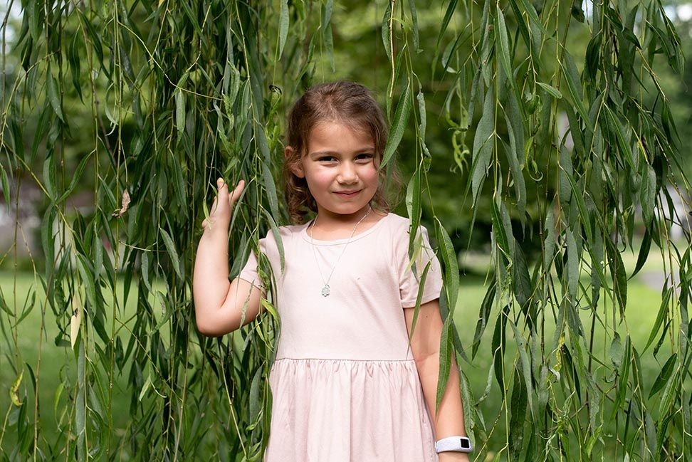 little girl standing beneath a weeping willow tree