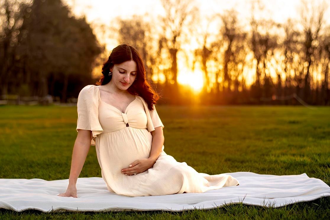 maternity photo session of pregnant women sitting in a field at sunset