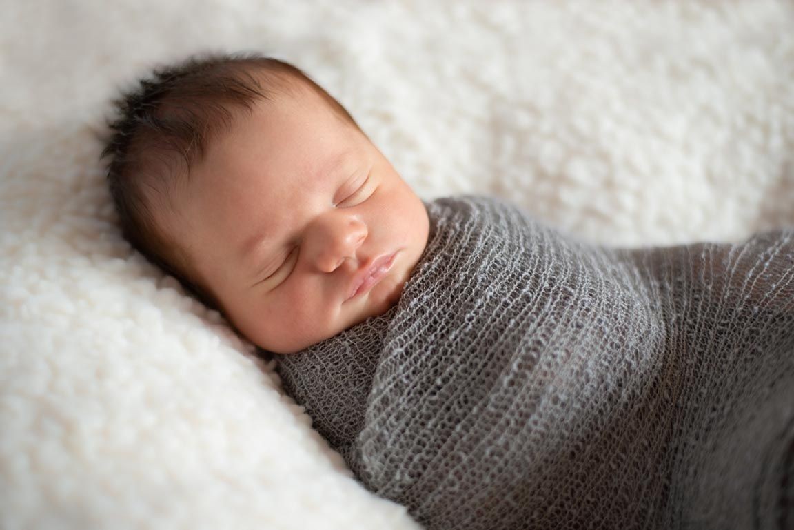 swaddled newborn baby sleeping on white blanket