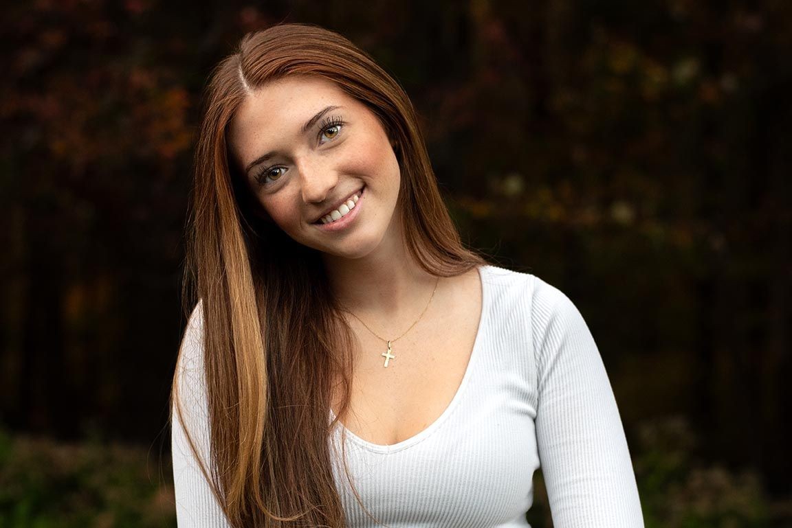 high school girl with brown hair brown eyes wearing a white shirt and cross necklace