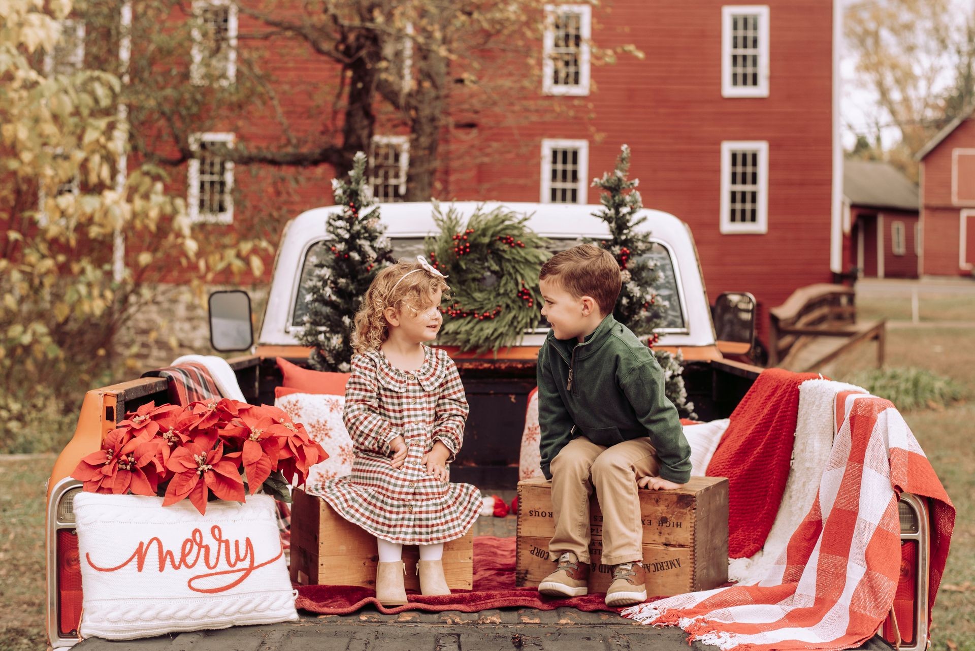 Smiling children sitting on truck bed decorated with holiday greens and red accents.